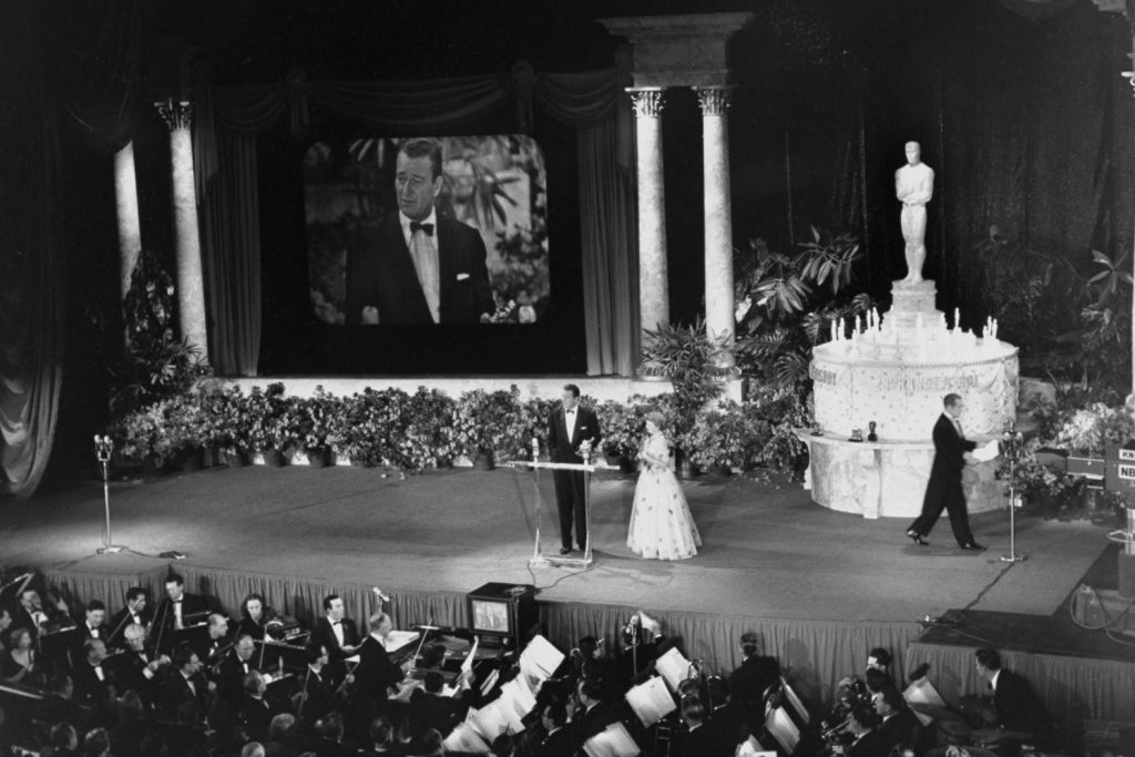 John Wayne accepts the Best Director Oscar from Olivia DeHavillan for an absent John Ford during the 25th annual Academy Awards in 1953